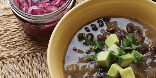 A bowl of black bean soup garnished with lime-pickled red onion and avocado