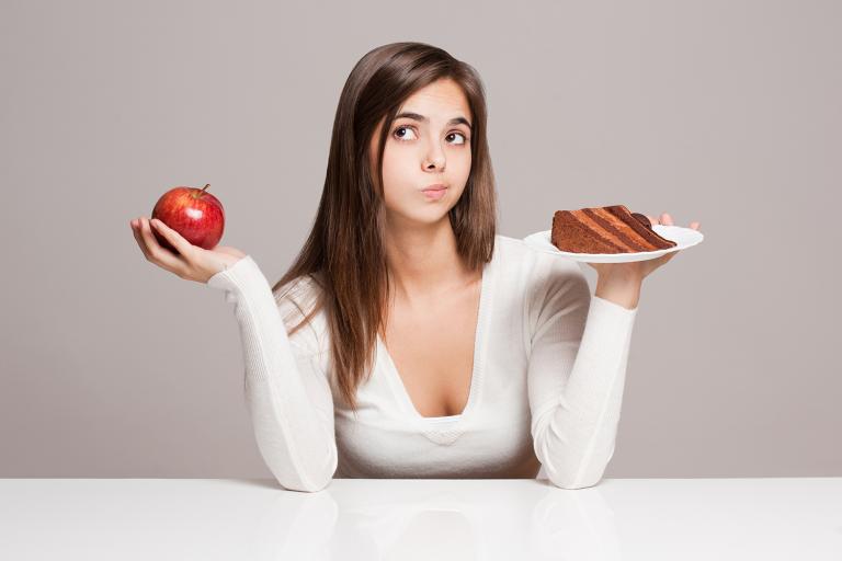 a young woman choosing between an apple and a slice of cake